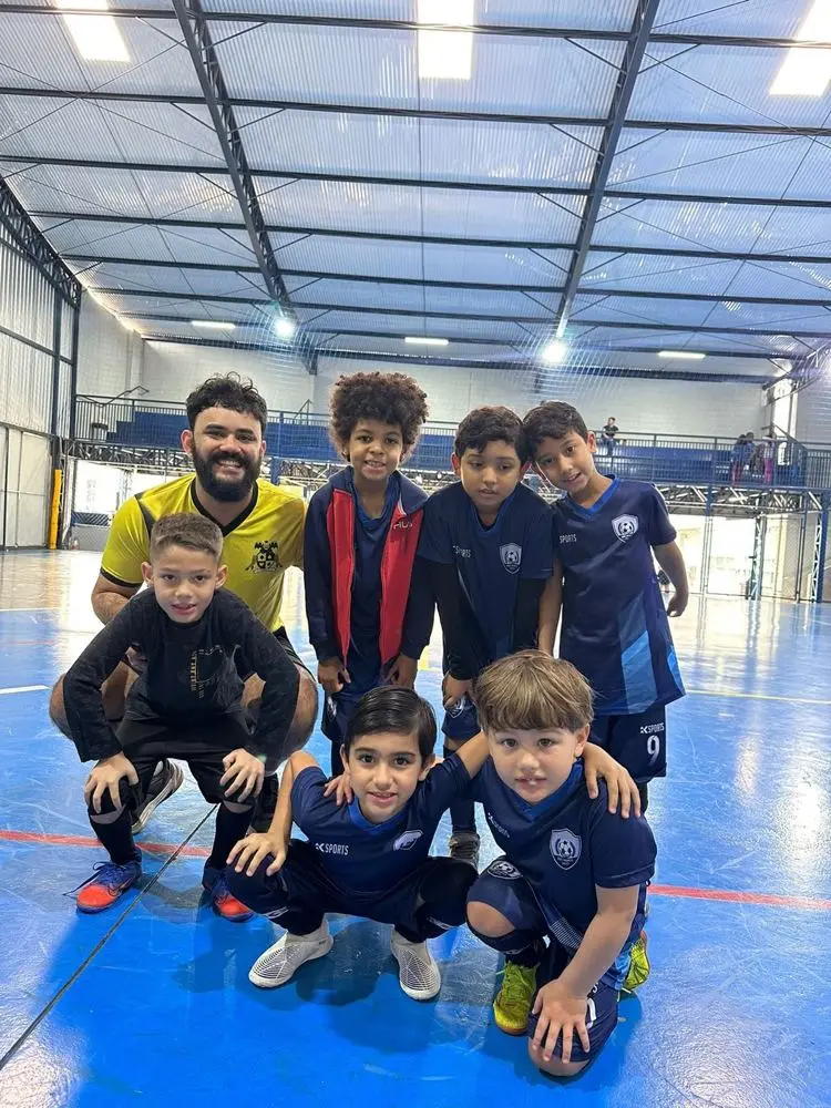 Professor e alunos de futsal posando juntos em uma quadra coberta