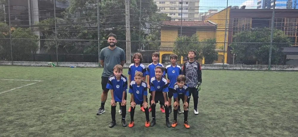 Turma de alunos uniformizados com o professor em um campo de grama sintética
